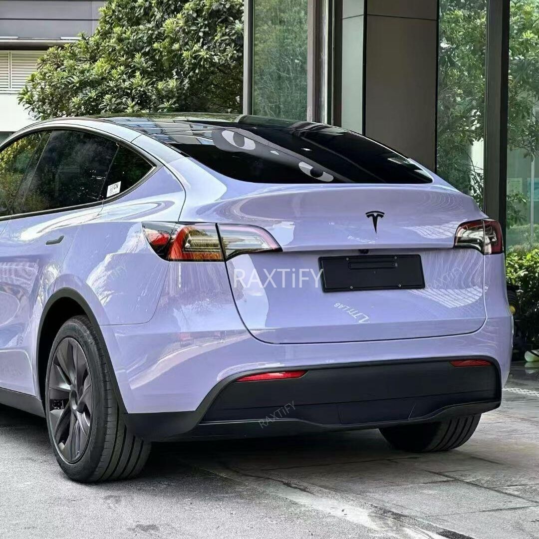 Back view of a Tesla in Gloss Victoria’s Secret Purple Vinyl Wrap parked in front of a building with greenery.