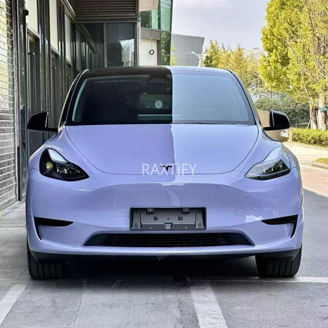 Front view of a Tesla in Gloss Victoria’s Secret Purple Vinyl Wrap parked on a street with a building and trees in the background.